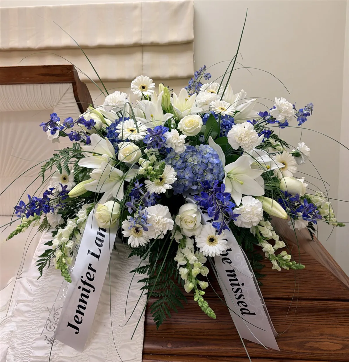 Blue and white casket spray with lilies, roses, and delphinium